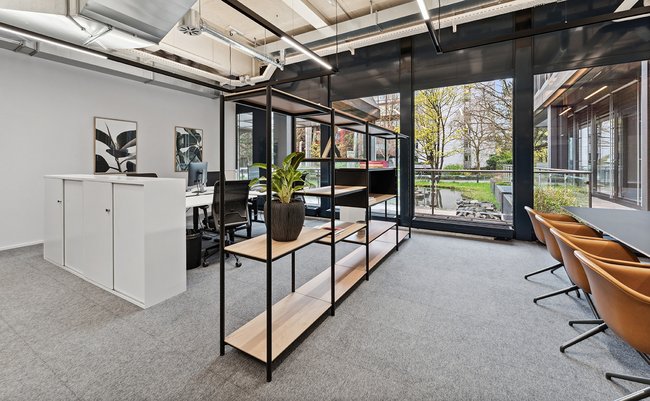 Büro im Erdgeschoss mit Blick auf Innenhof mit Garten. Vier Arbeitsplätze, ein offenes Regal als Raumtrenner und ein Besprechungstisch
